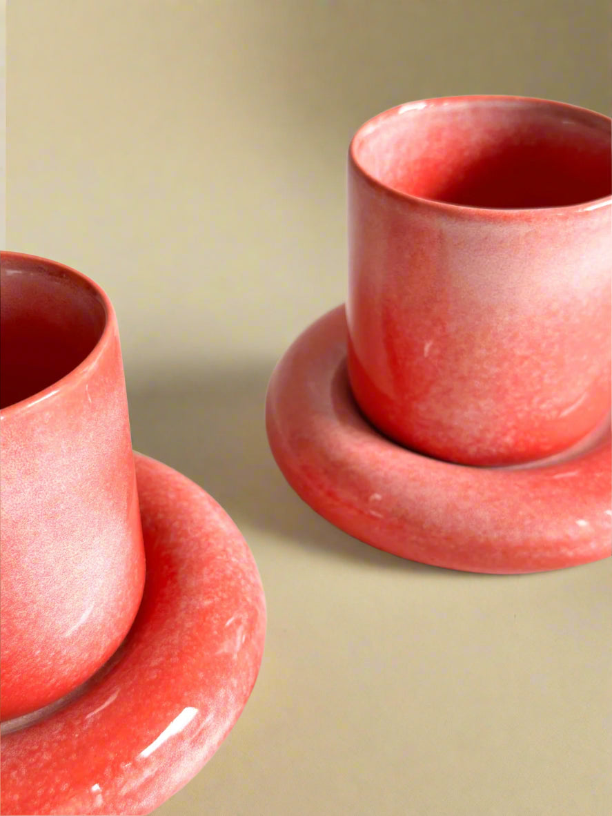 a couple of red cups and saucers on a table