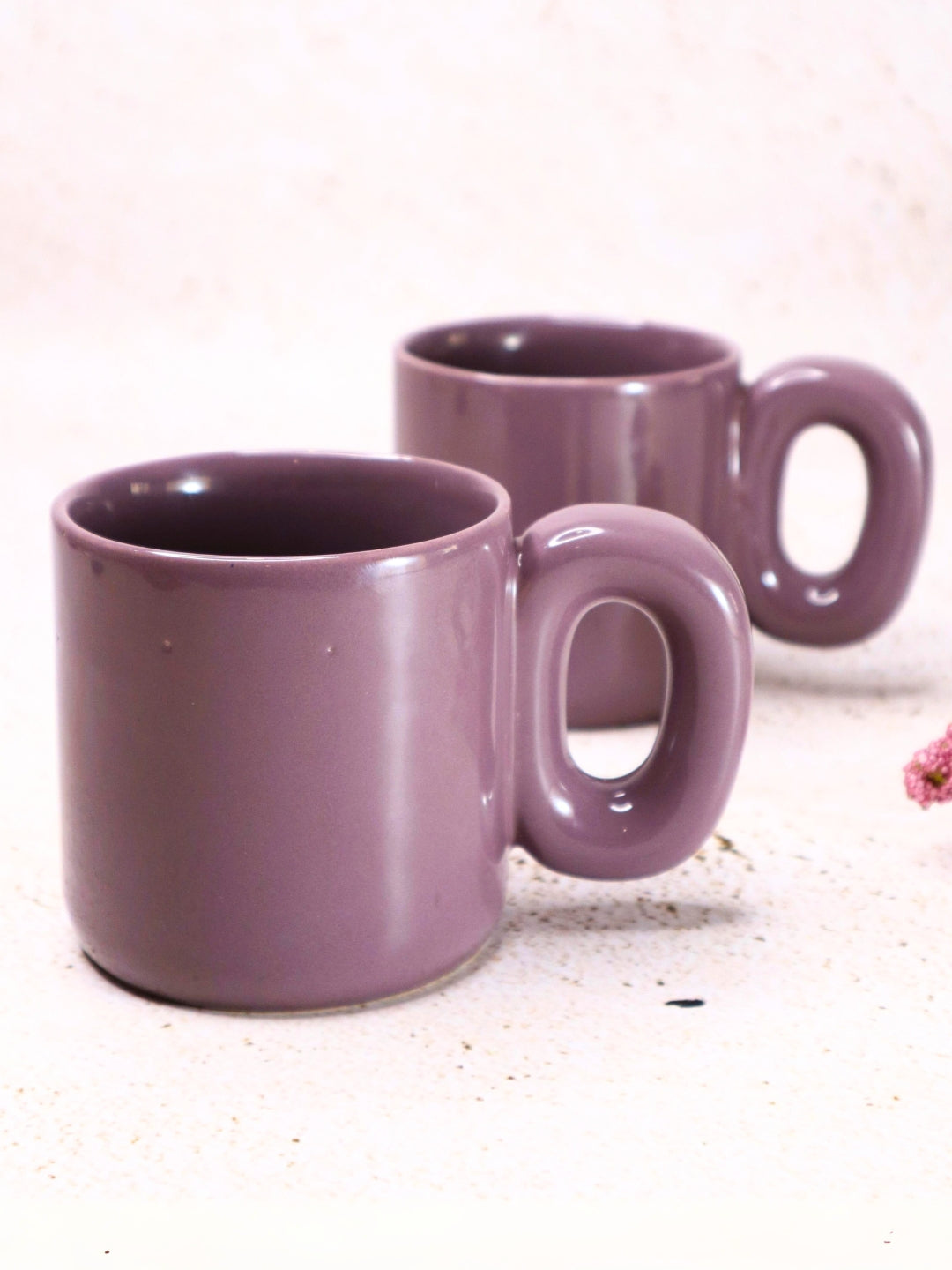 two purple coffee mugs sitting next to a pink flower