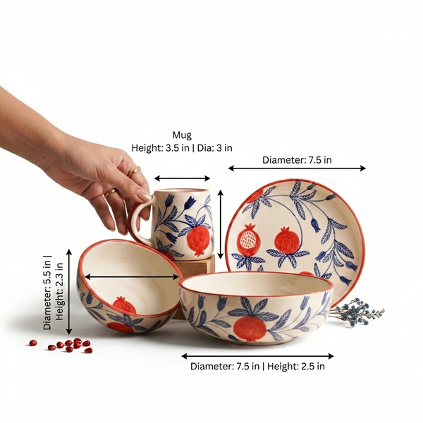 Ceramic tableware set with a mug, bowl, and plate decorated with a blue botanical leaf pattern and red pomegranate motifs on a cream background, shown with hand and dimension arrows on a white background.