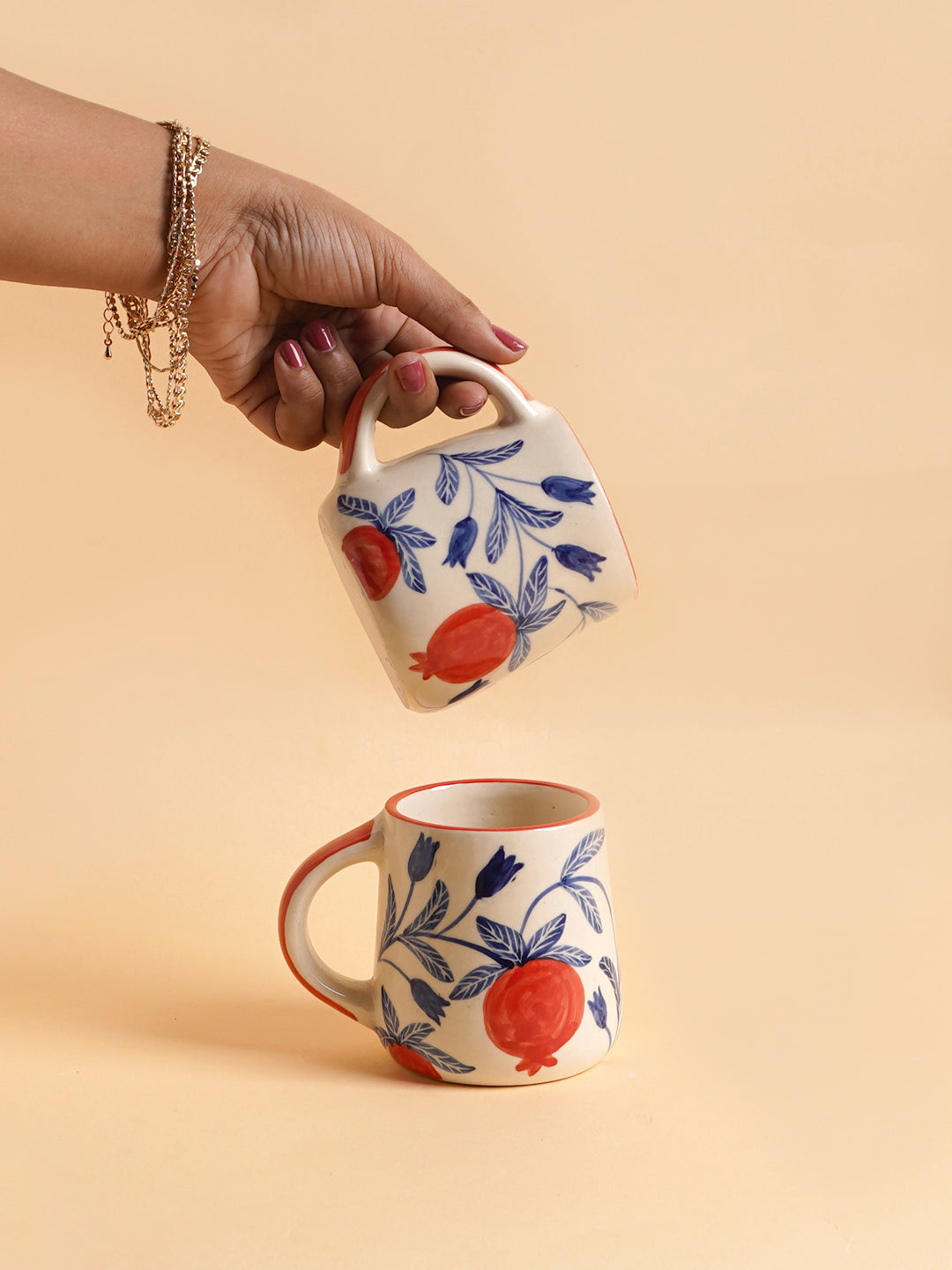 A person holding a ceramic coffee mug with a floral pattern, with another ceramic mug placed on the surface.