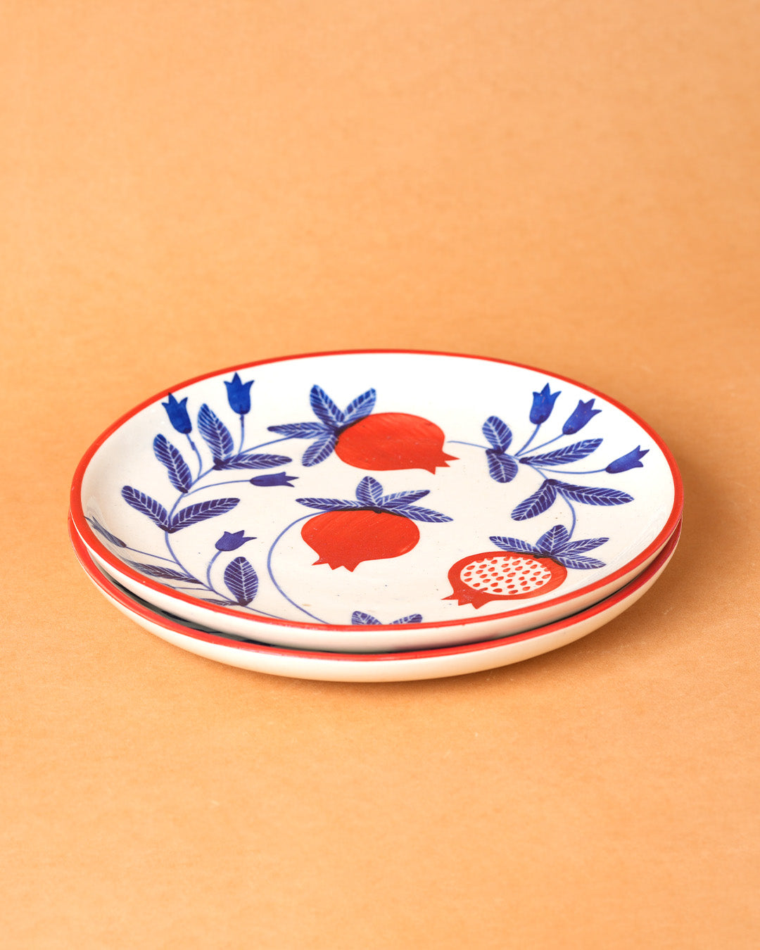 Stack of ceramic plates with blue floral and red fruit design on a beige background