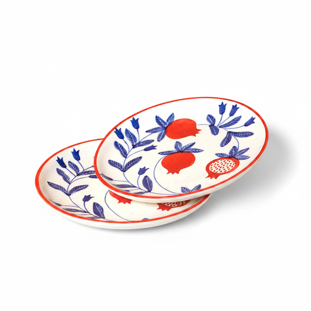 Two decorative plates with blue floral patterns and red pomegranate designs on a beige background