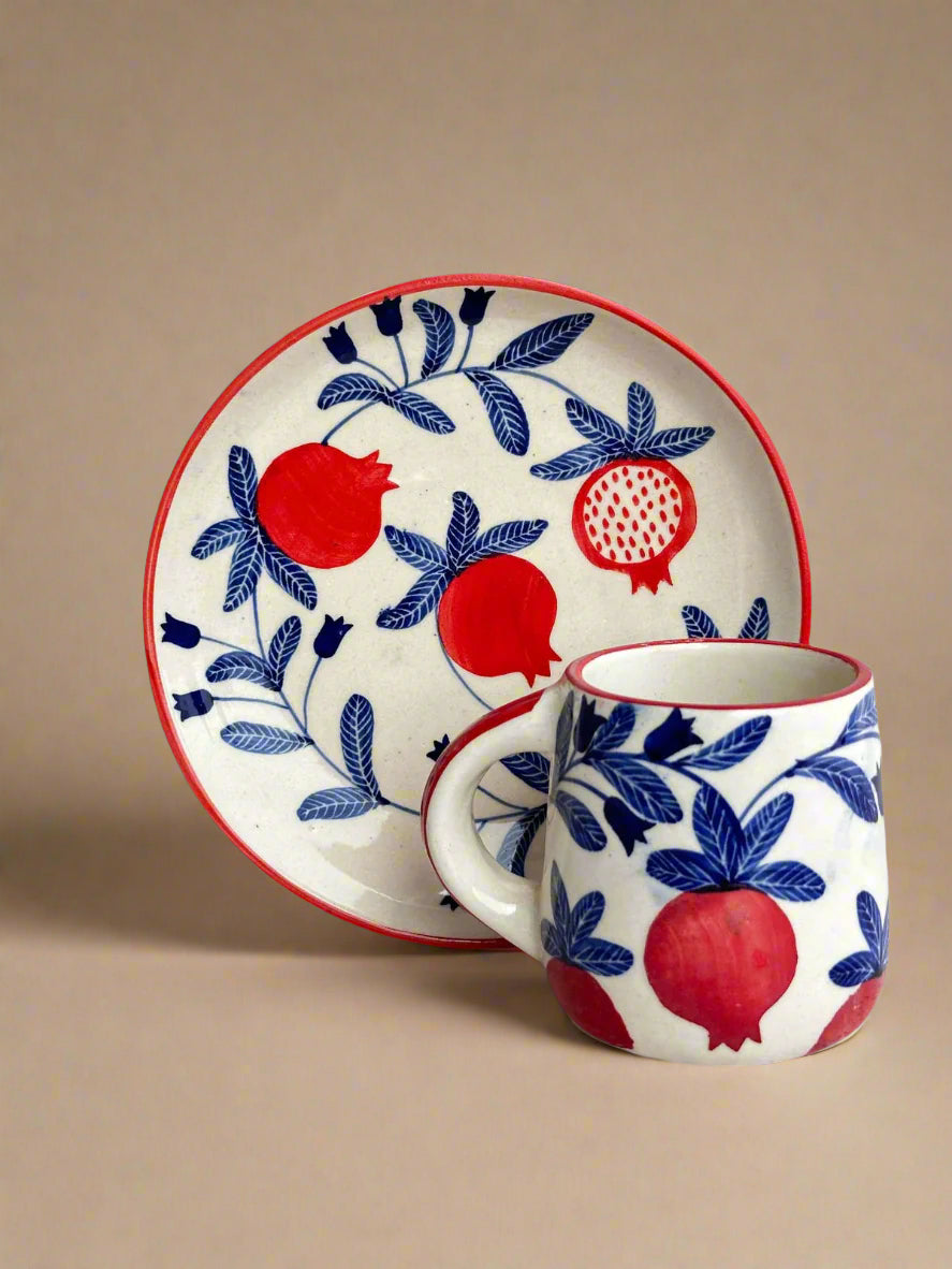 A ceramic plate and mug set with a red and blue pomegranate design on a white background.