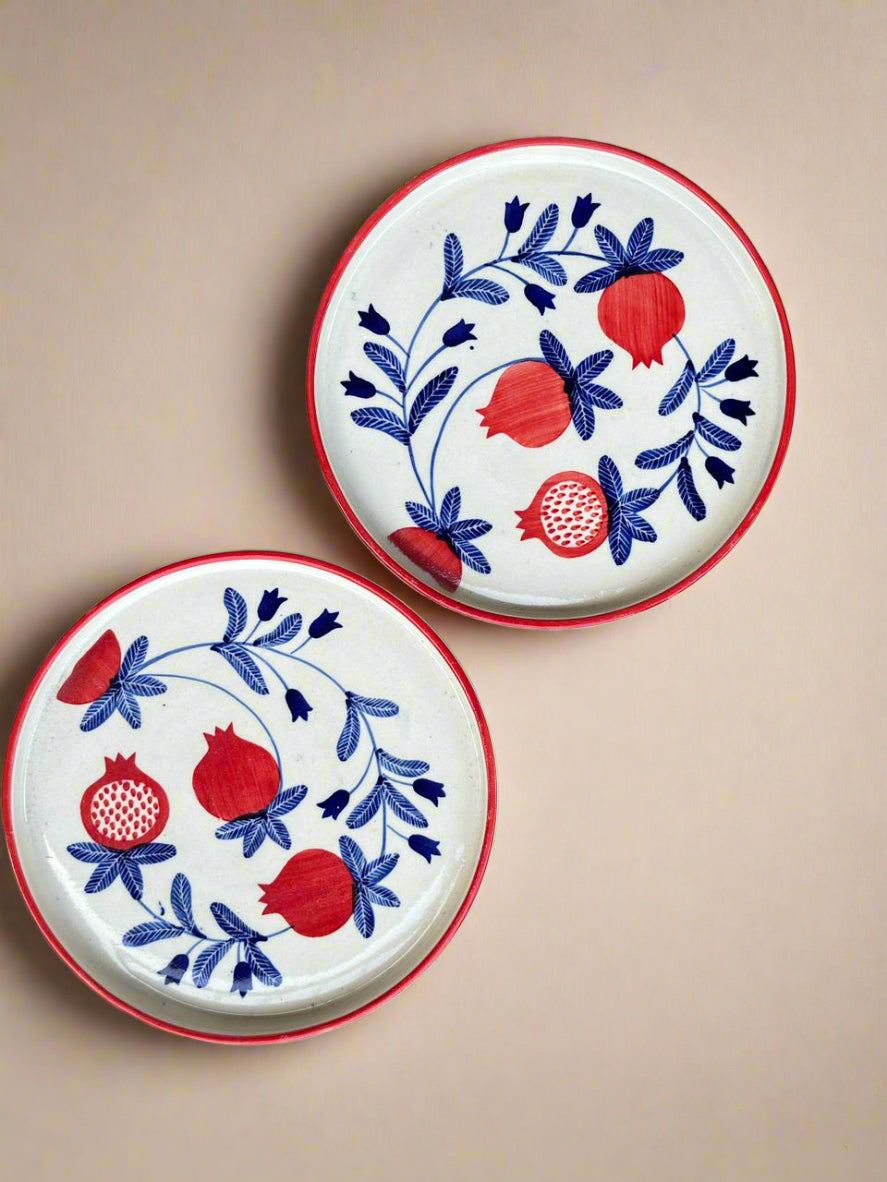 Two ceramic plates with red and blue floral and pomegranate designs on a beige background