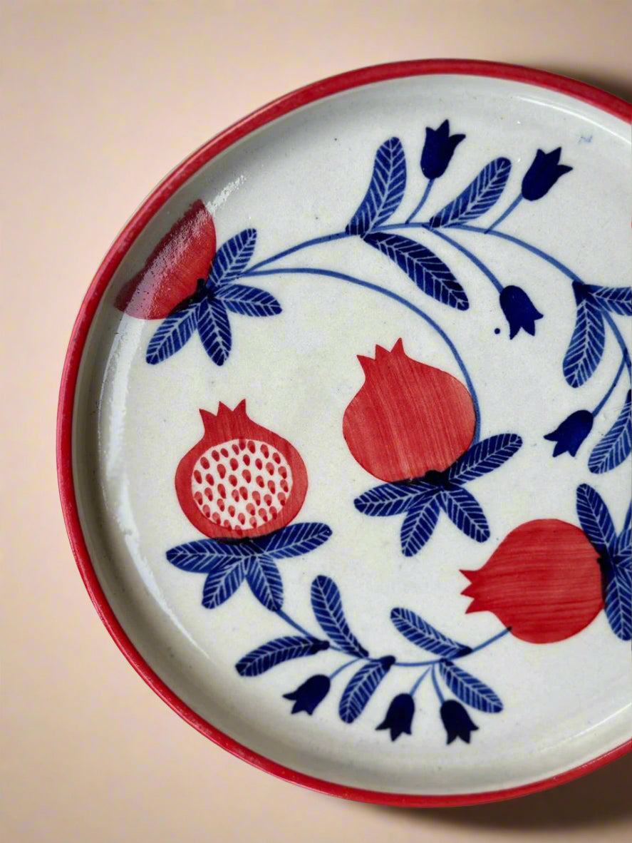 Decorative plate with red pomegranates and blue floral patterns on a beige background