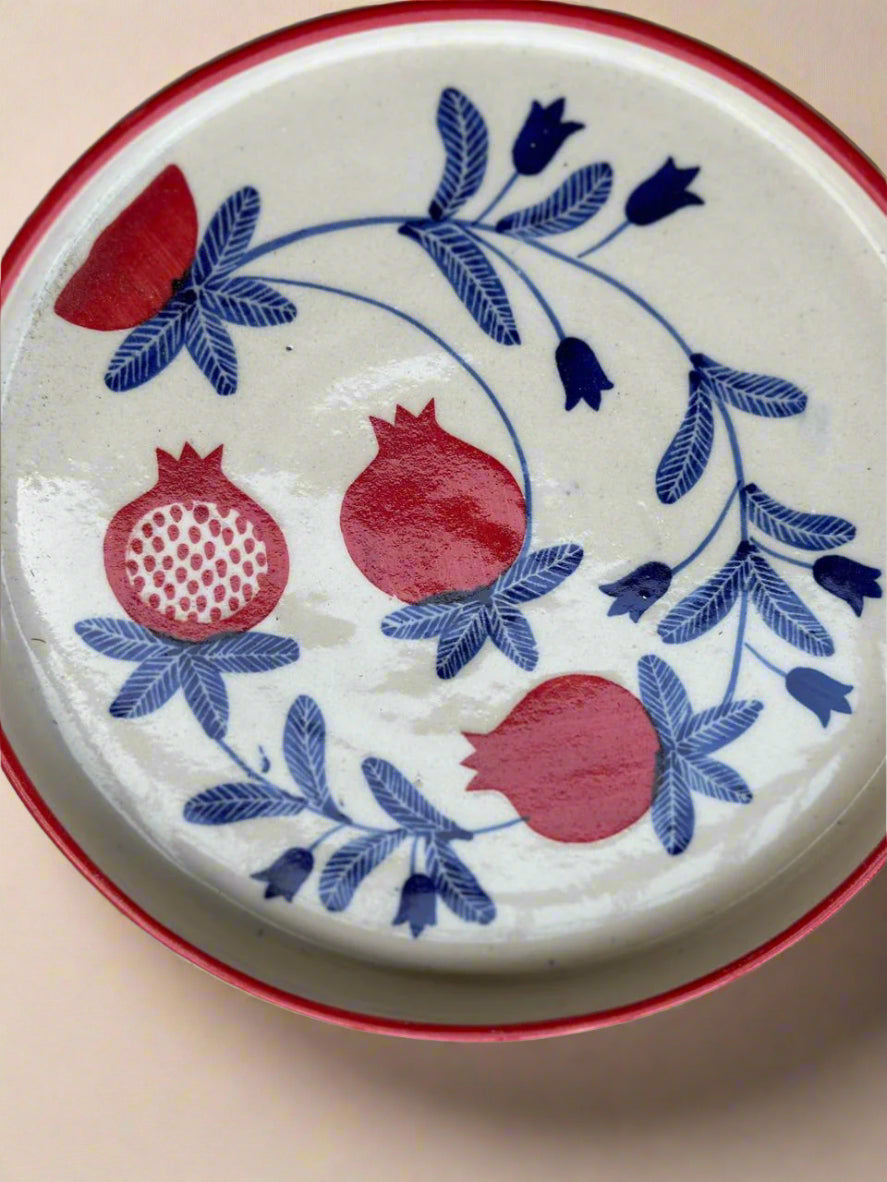 Ceramic plate with red pomegranate and blue floral design on a white background