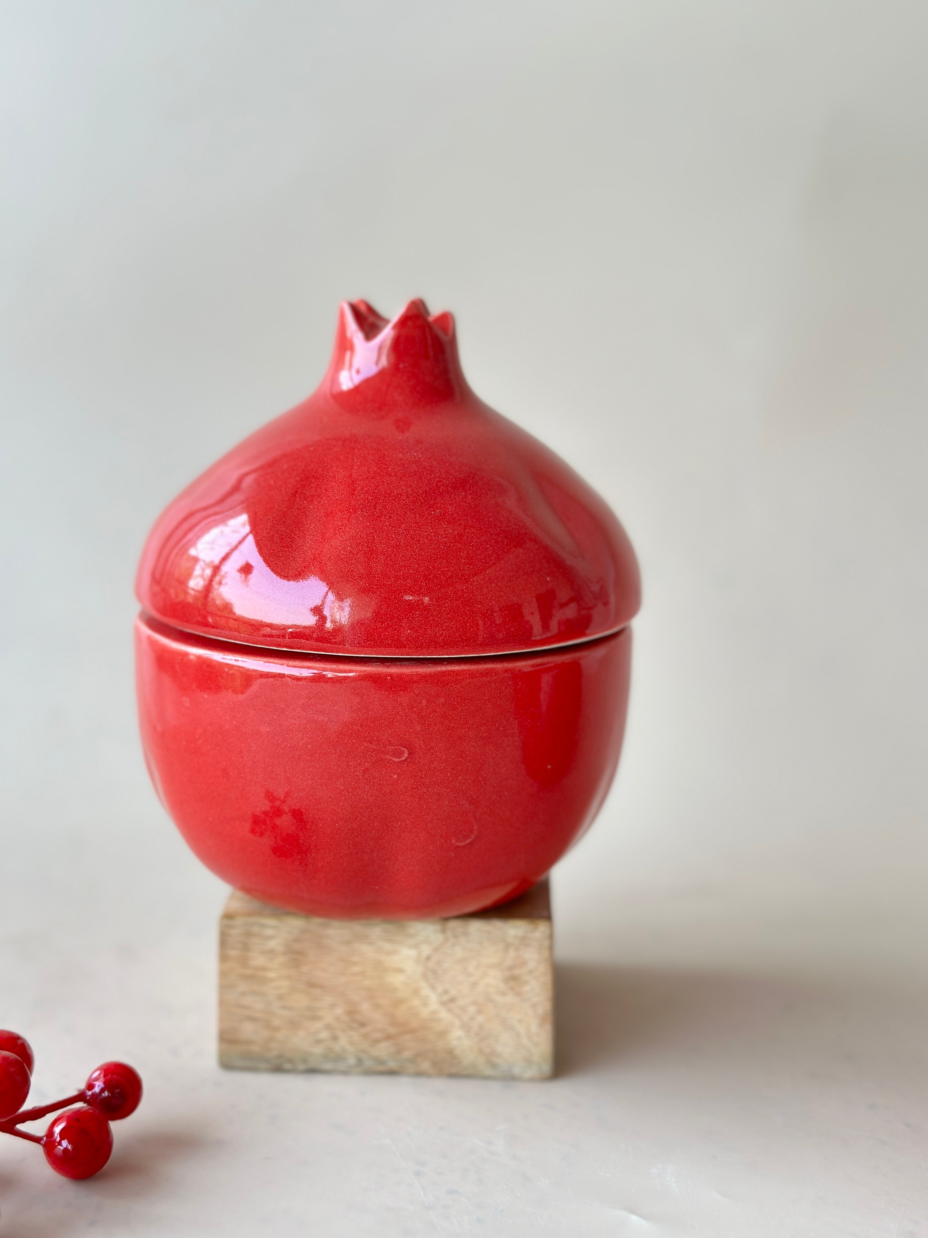 A red ceramic jar designed to resemble a pomegranate, placed on a wooden stand, with a small amount of white residue visible on the surface.