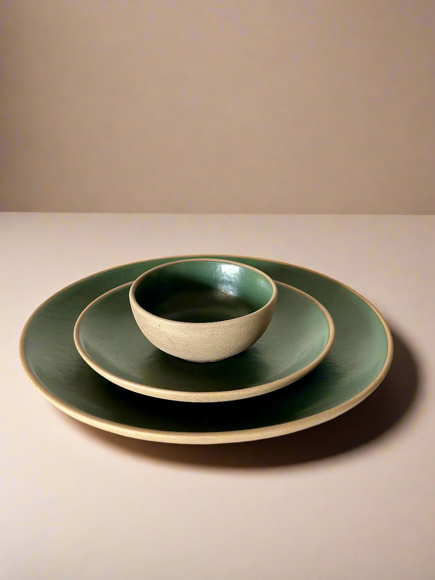 Set of green ceramic plates and bowl on a light surface with a white background