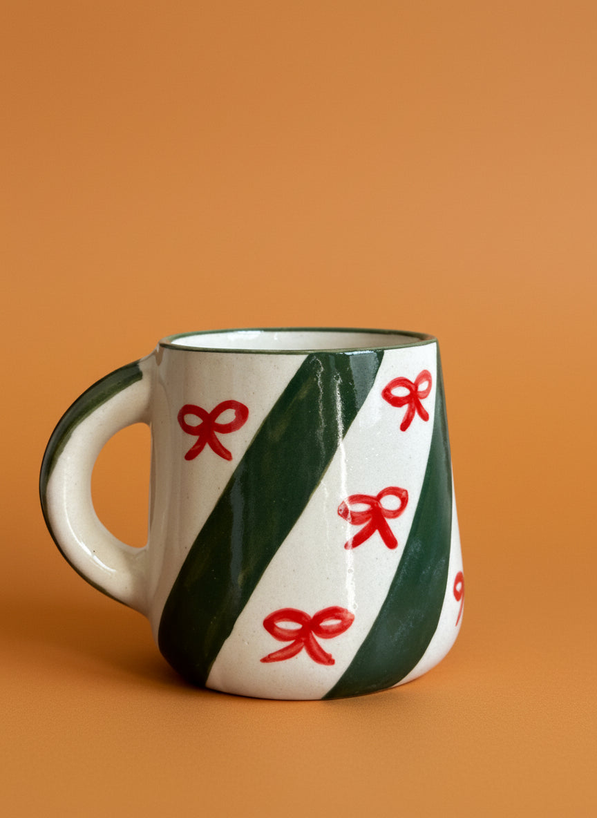 Ceramic mug with green stripes and red bows on an orange background