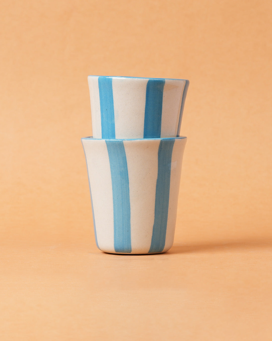 Two ceramic cups with blue stripes on a beige background