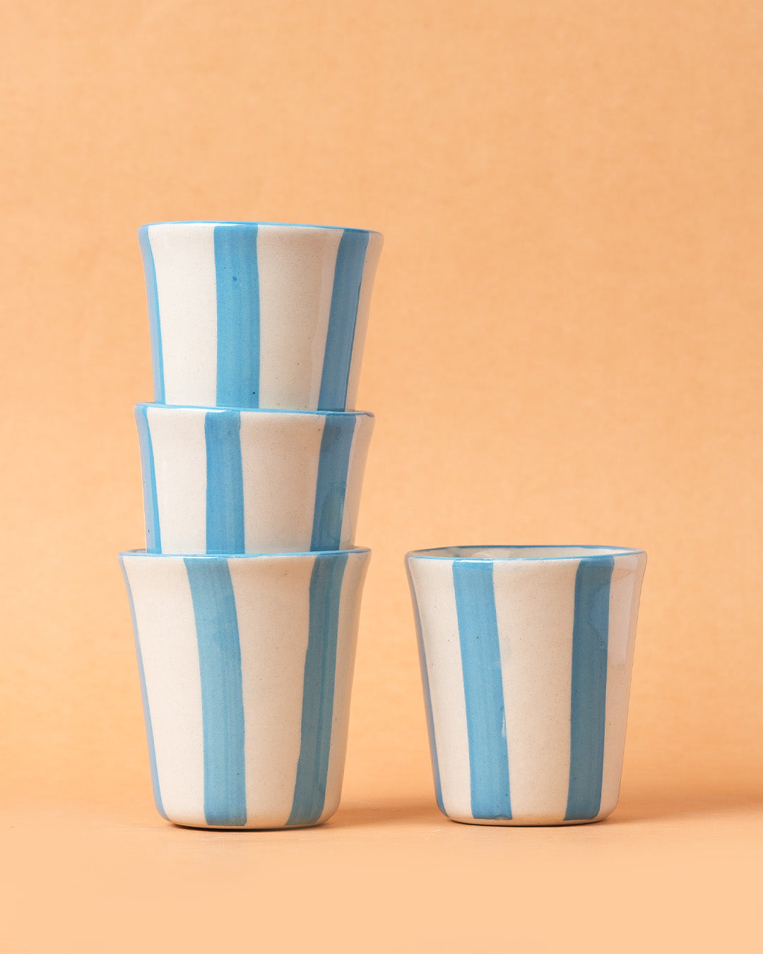 Stack of ceramic cups with blue and beige stripes on a peach background