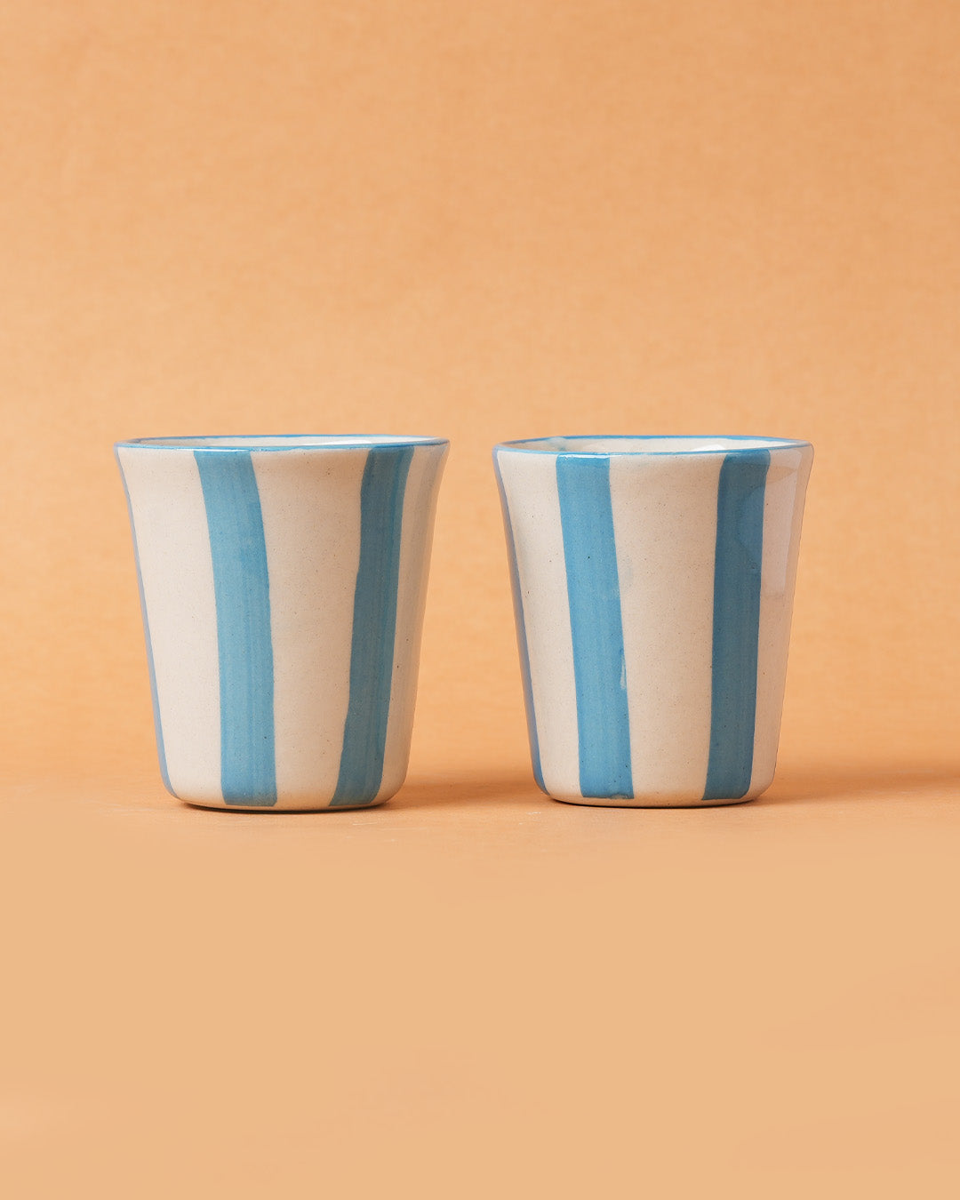 Two ceramic cups with blue stripes on a beige background