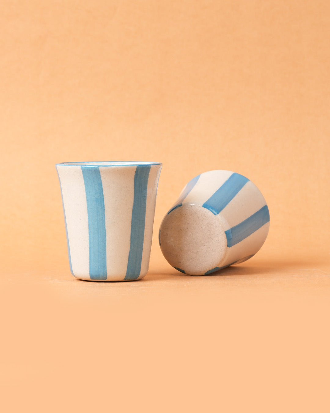 Ceramic cup and ball with blue stripes on a peach background