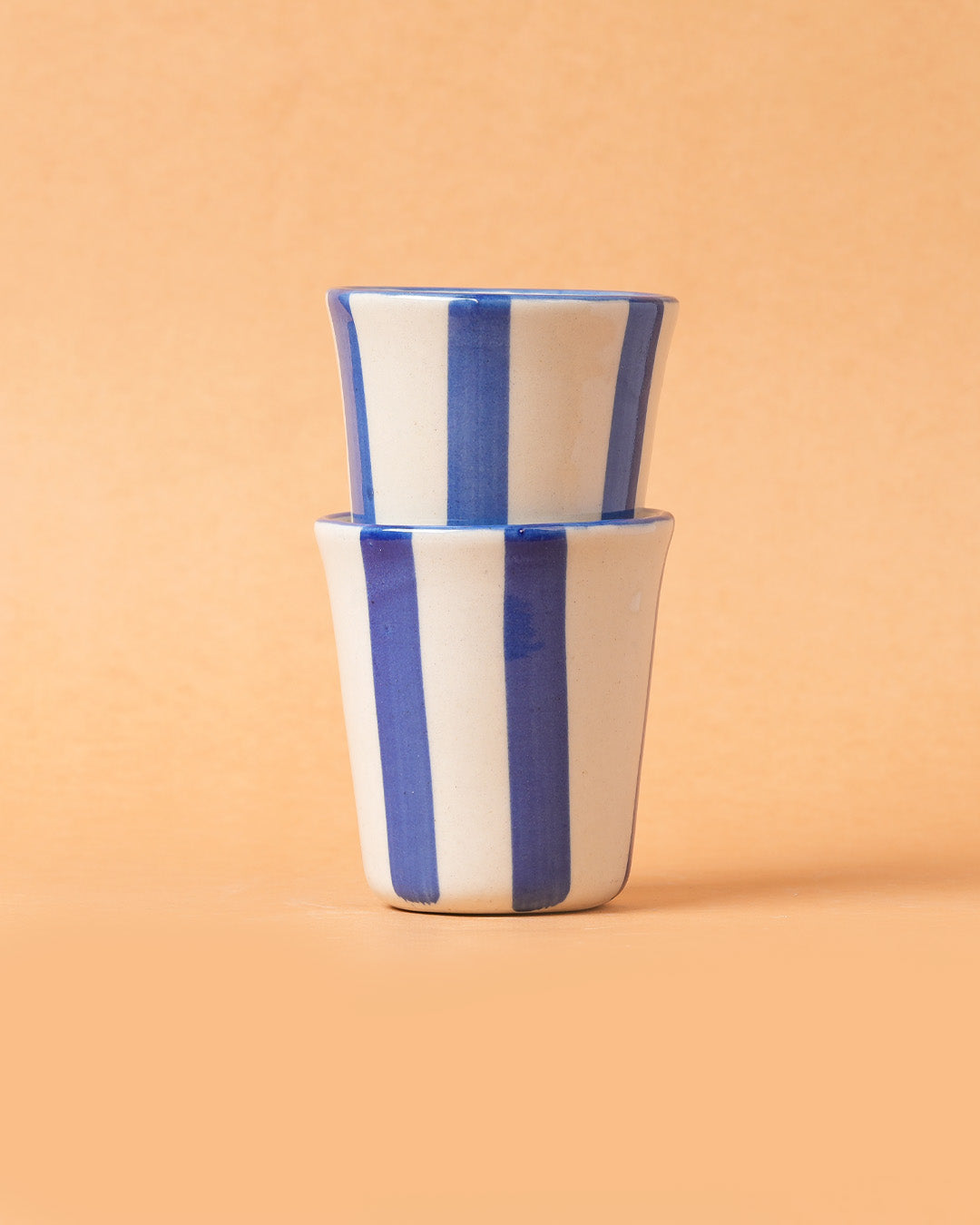 Two stacked ceramic cups with blue and white stripes on a beige background