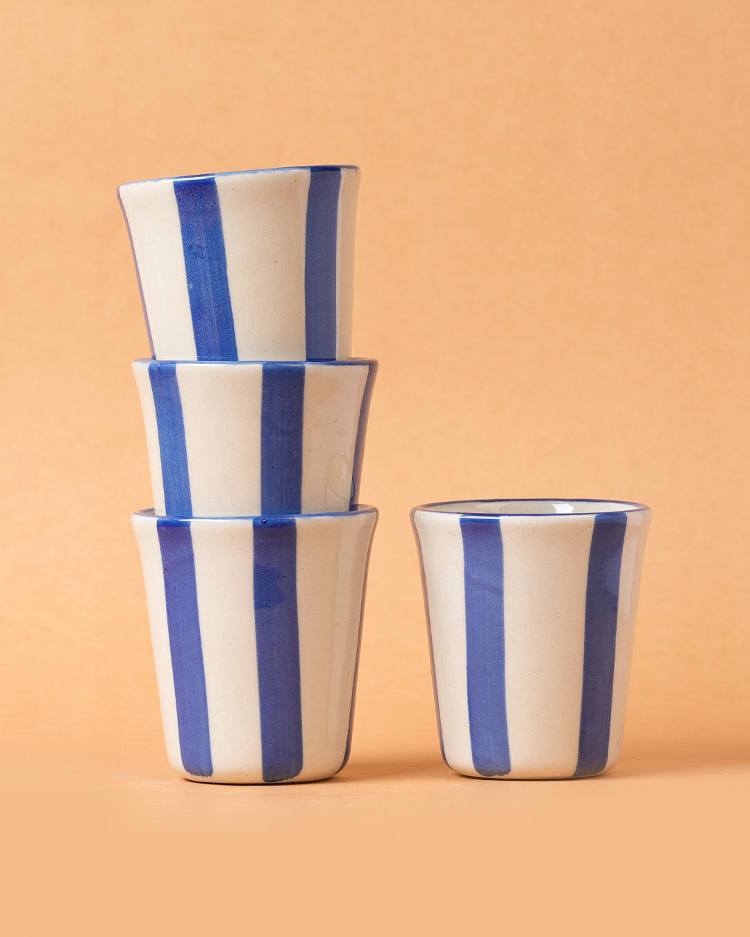 Stack of ceramic cups with blue stripes on a beige background