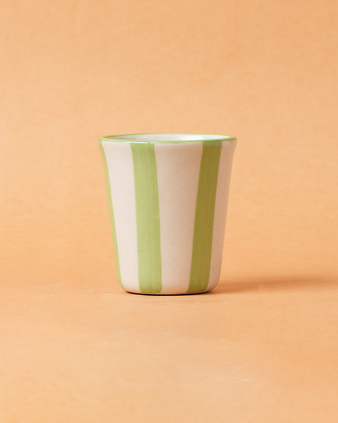 Ceramic cup with green and white stripes on a peach background