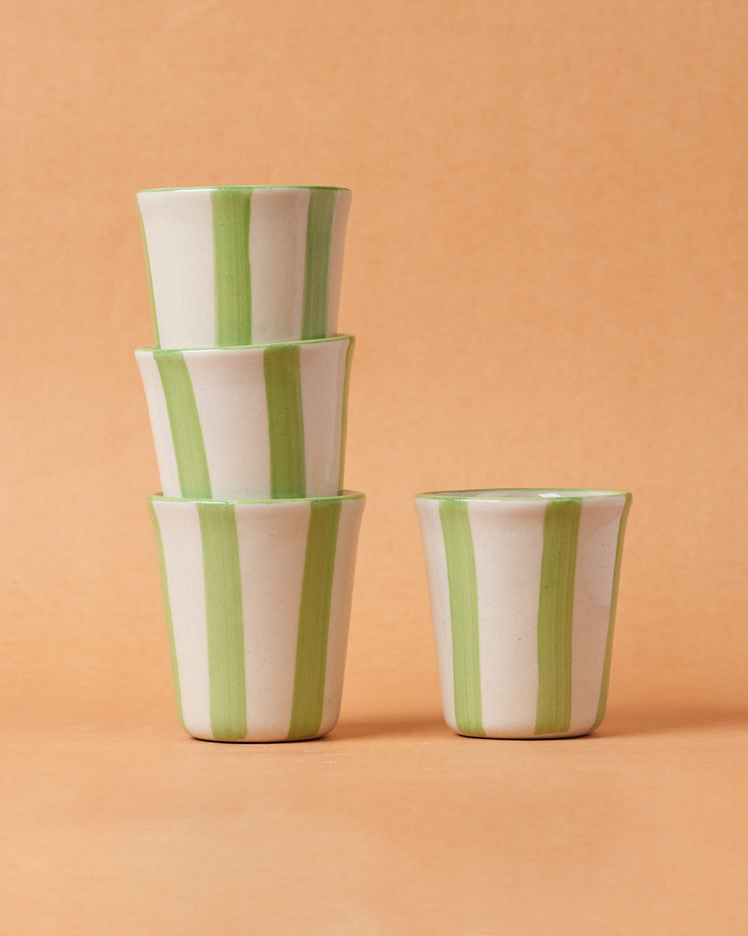 Stack of three ceramic cups with green and white stripes on a peach background