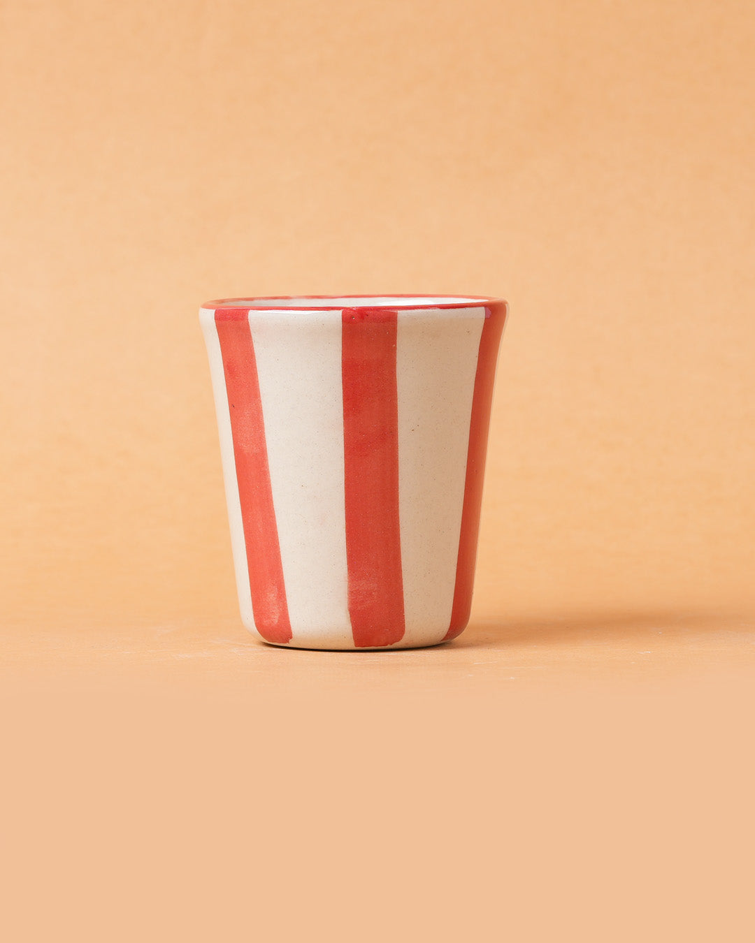 Ceramic cup with red and white stripes on a beige background
