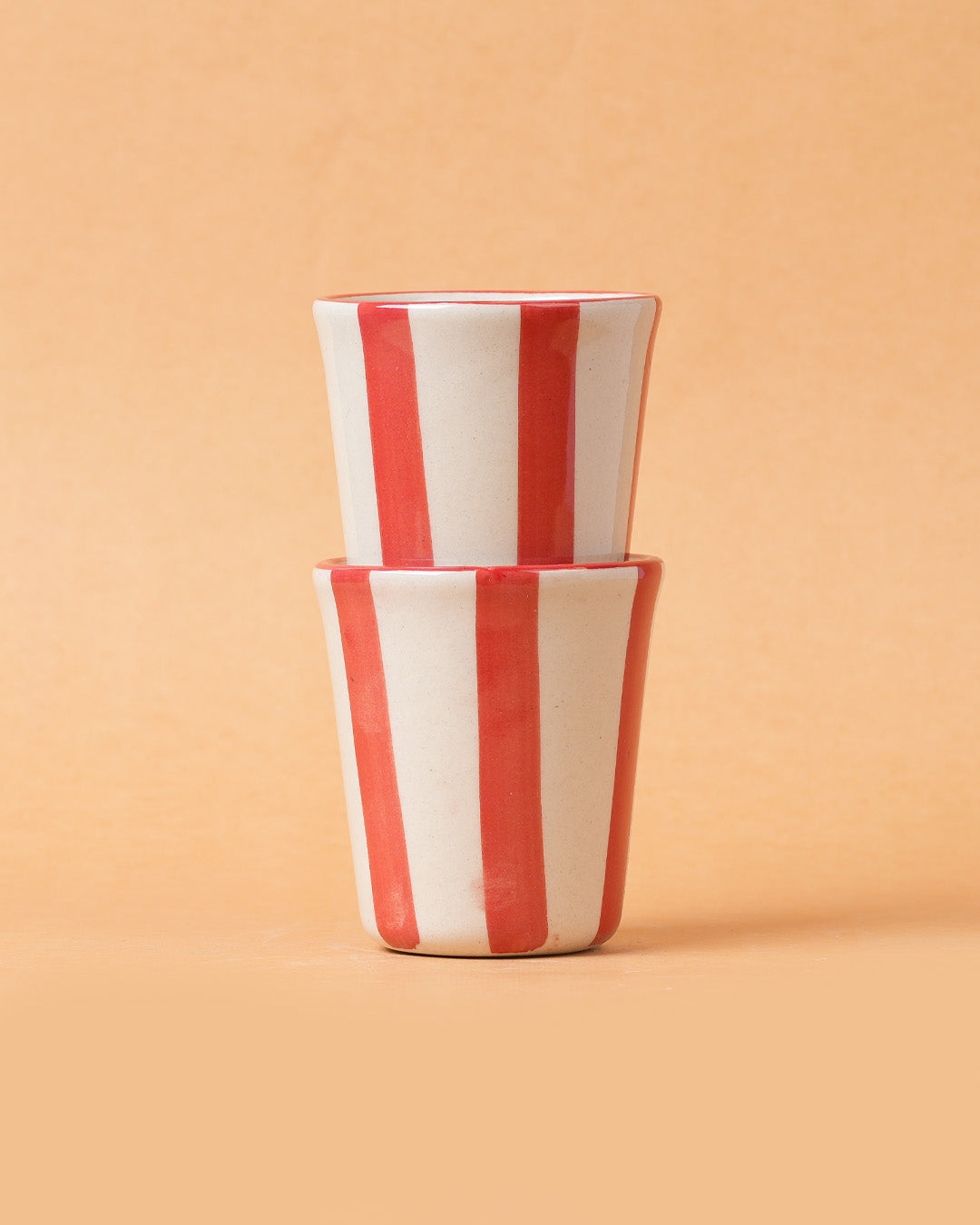 Two red and white striped ceramic cups on a beige background