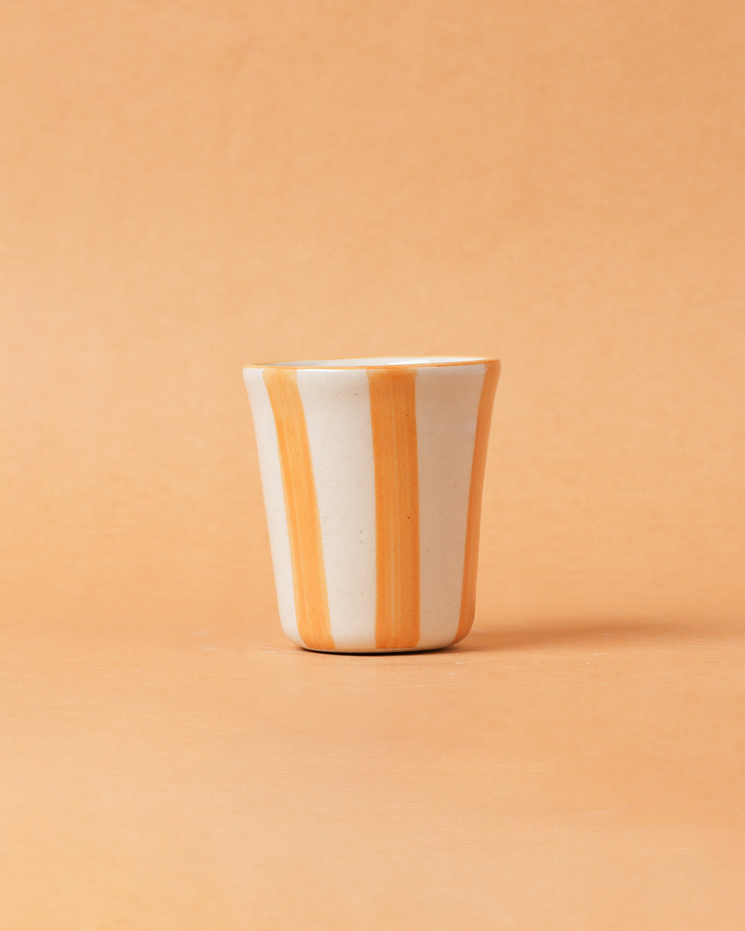 Ceramic cup with orange and white stripes on a peach background