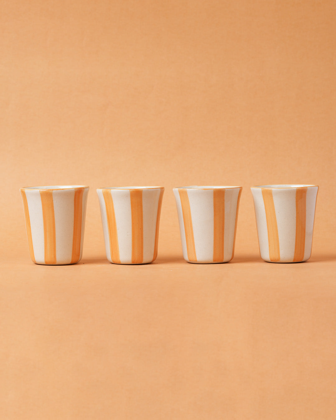 Four ceramic cups with orange and white stripes on a beige background