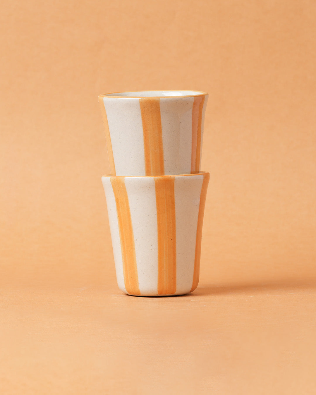 Two stacked ceramic cups with orange and white stripes on a peach background