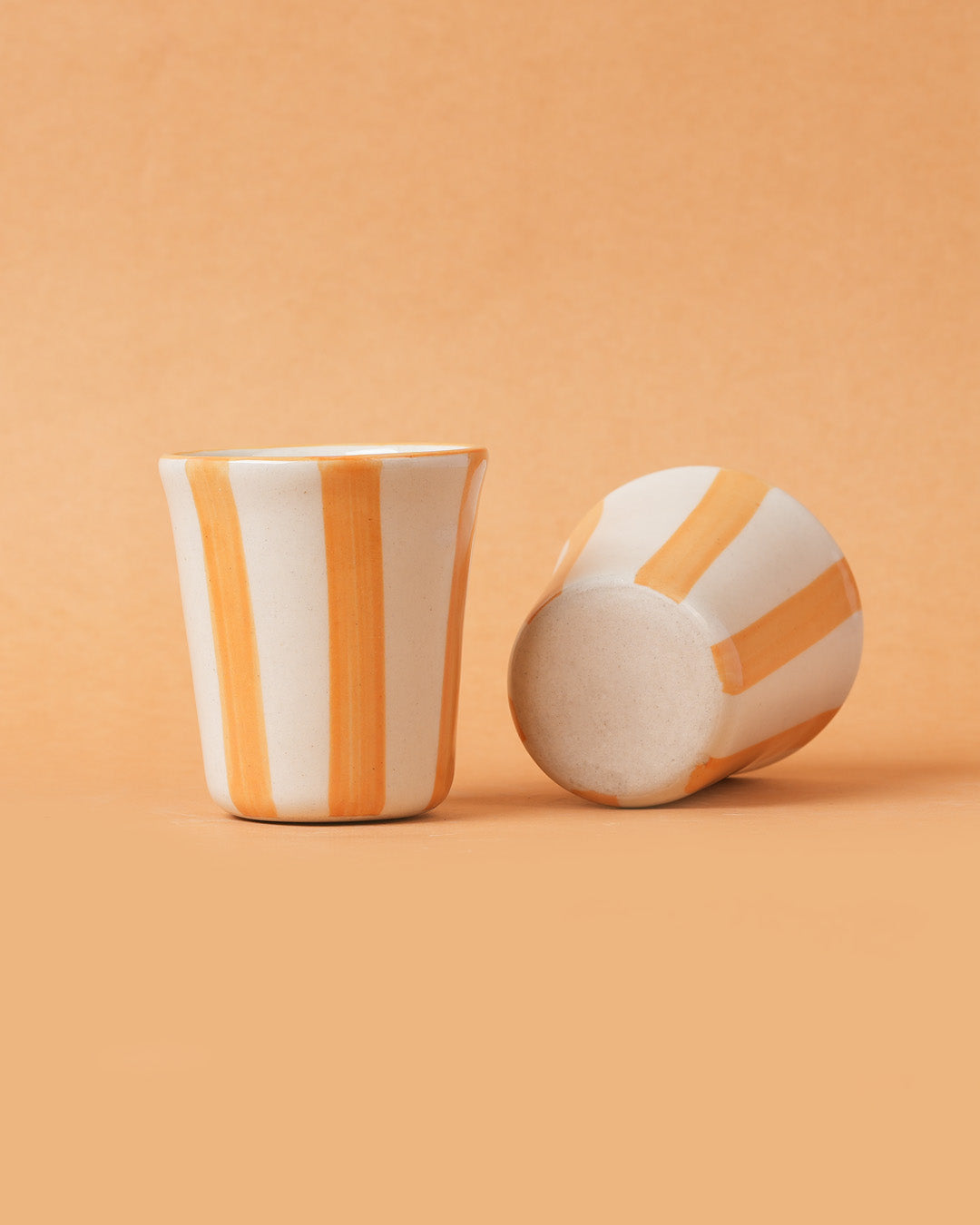 Two ceramic cups with orange and white stripes on a peach background