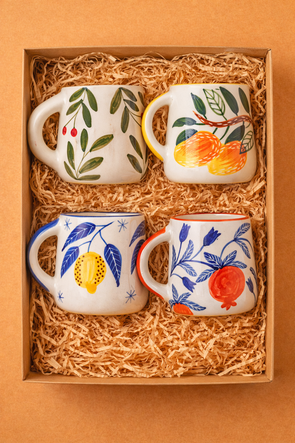 Set of four ceramic mugs with floral and fruit designs in a box with straw lining.