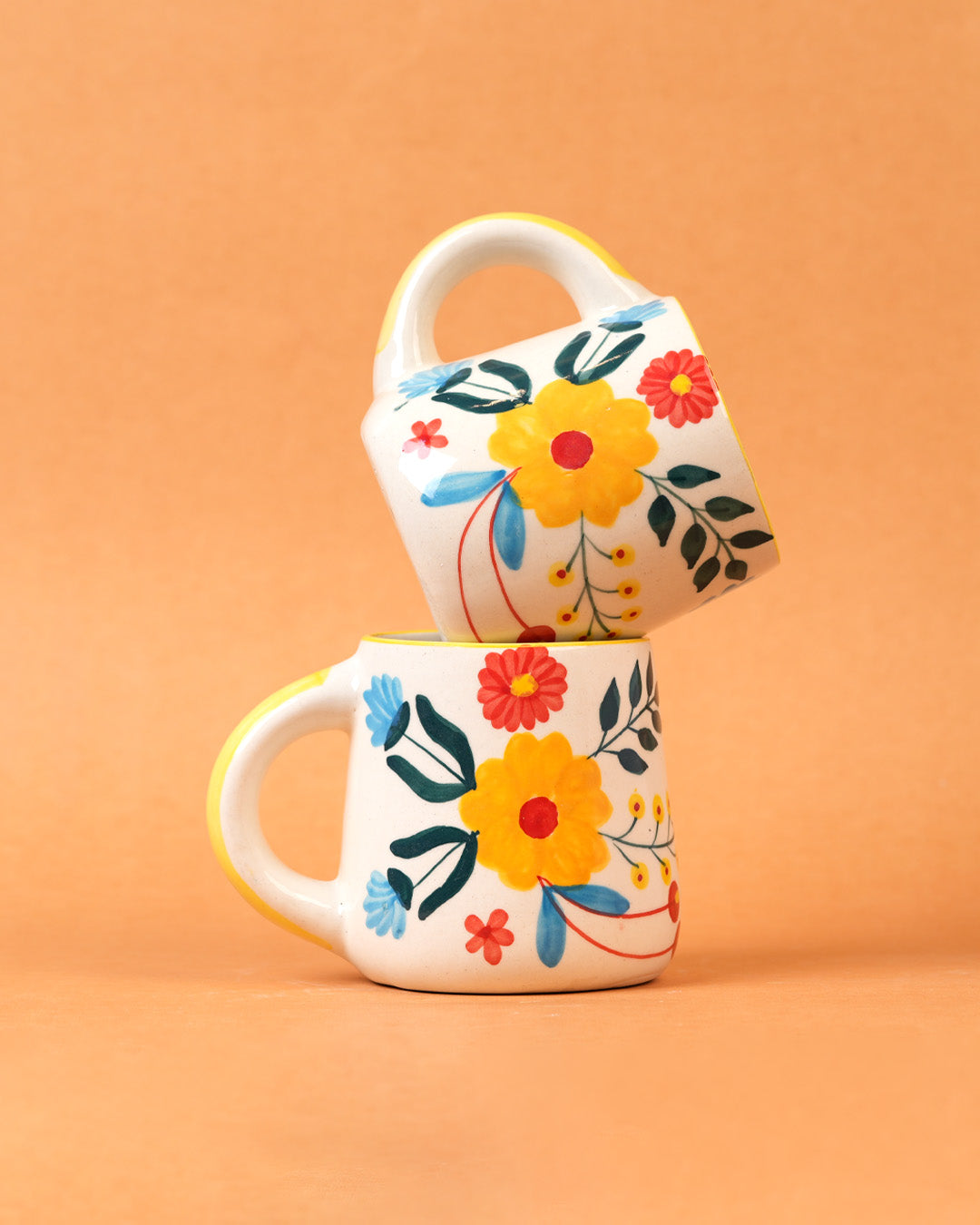 Two floral-patterned mugs stacked on an orange background