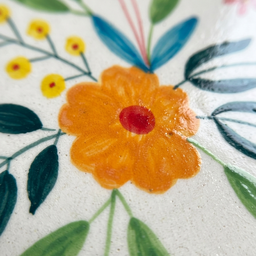 Close-up of a floral design with an orange flower and green leaves on a white background.