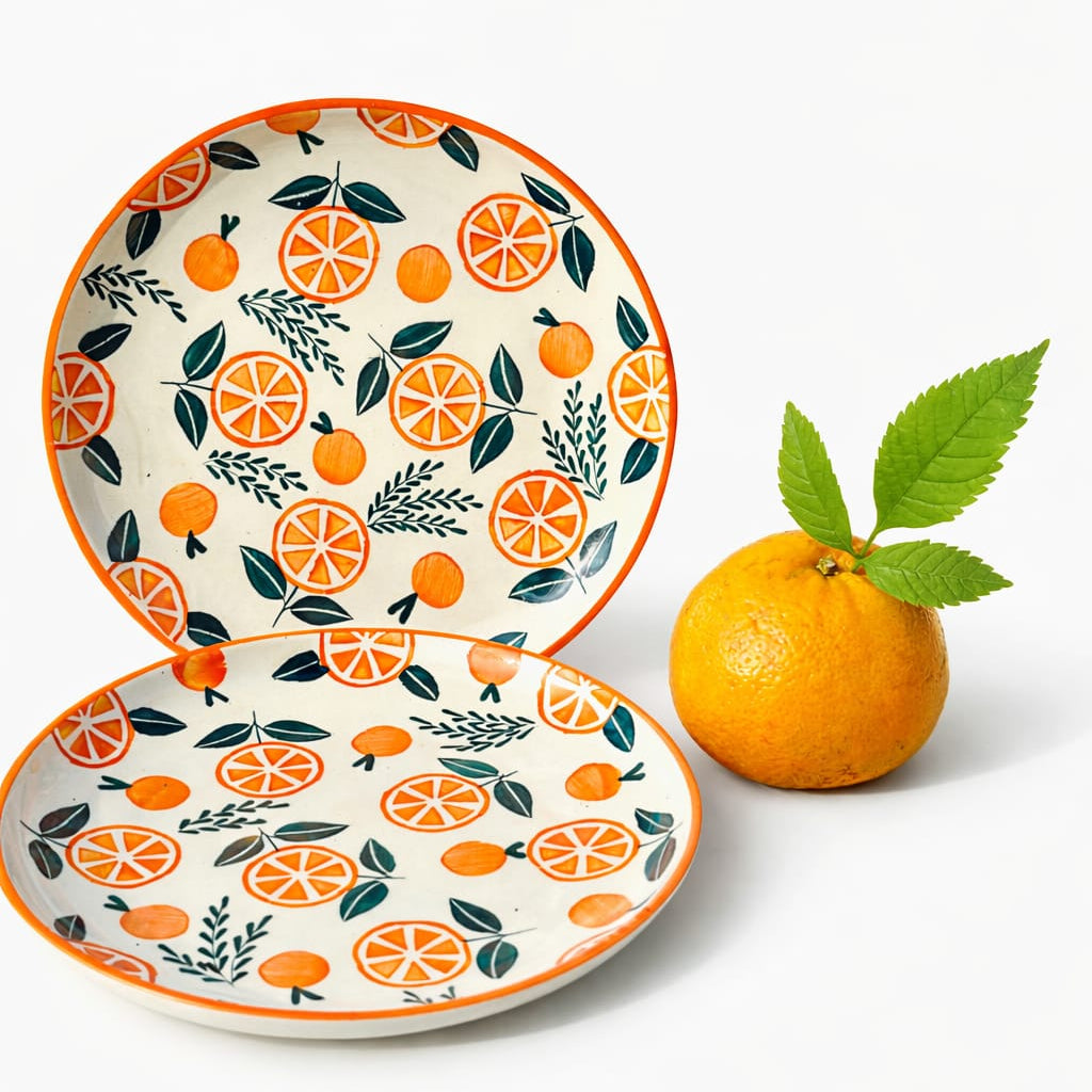 Two ceramic plates with orange and leaf pattern next to a real orange on a white background