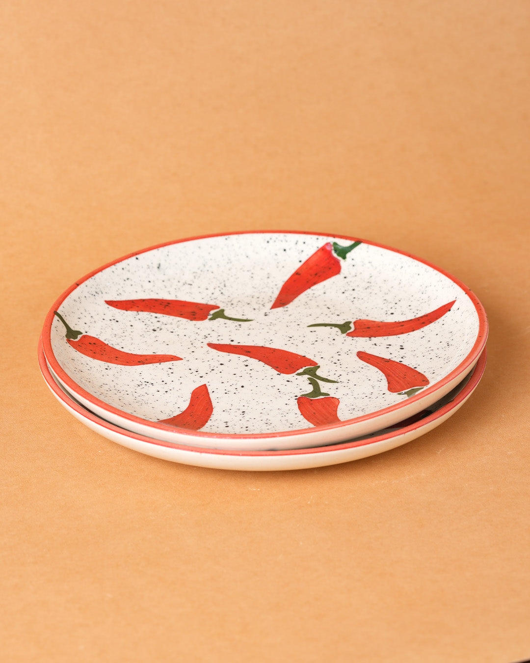 Two ceramic plates with red chili pepper pattern on a beige background