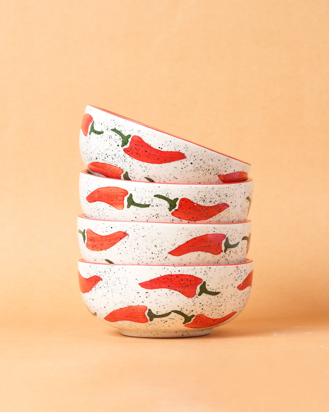 Set of four ceramic bowls with red chili pepper design on a beige background