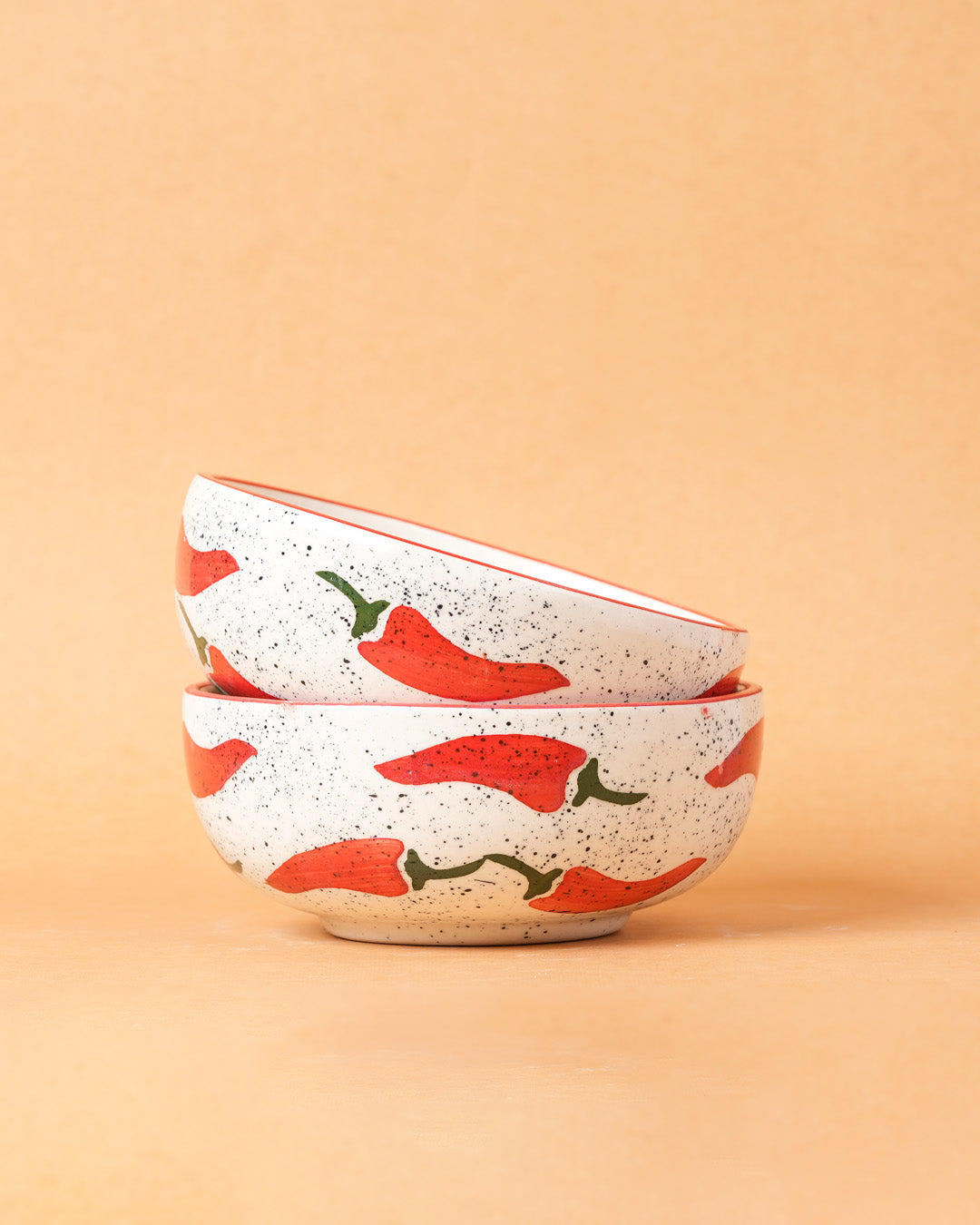 Two ceramic bowls with red chili pepper design on a beige background