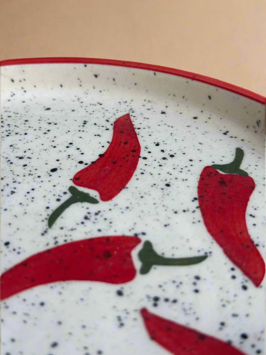 Speckled ceramic plate with red chili pepper design on a beige background