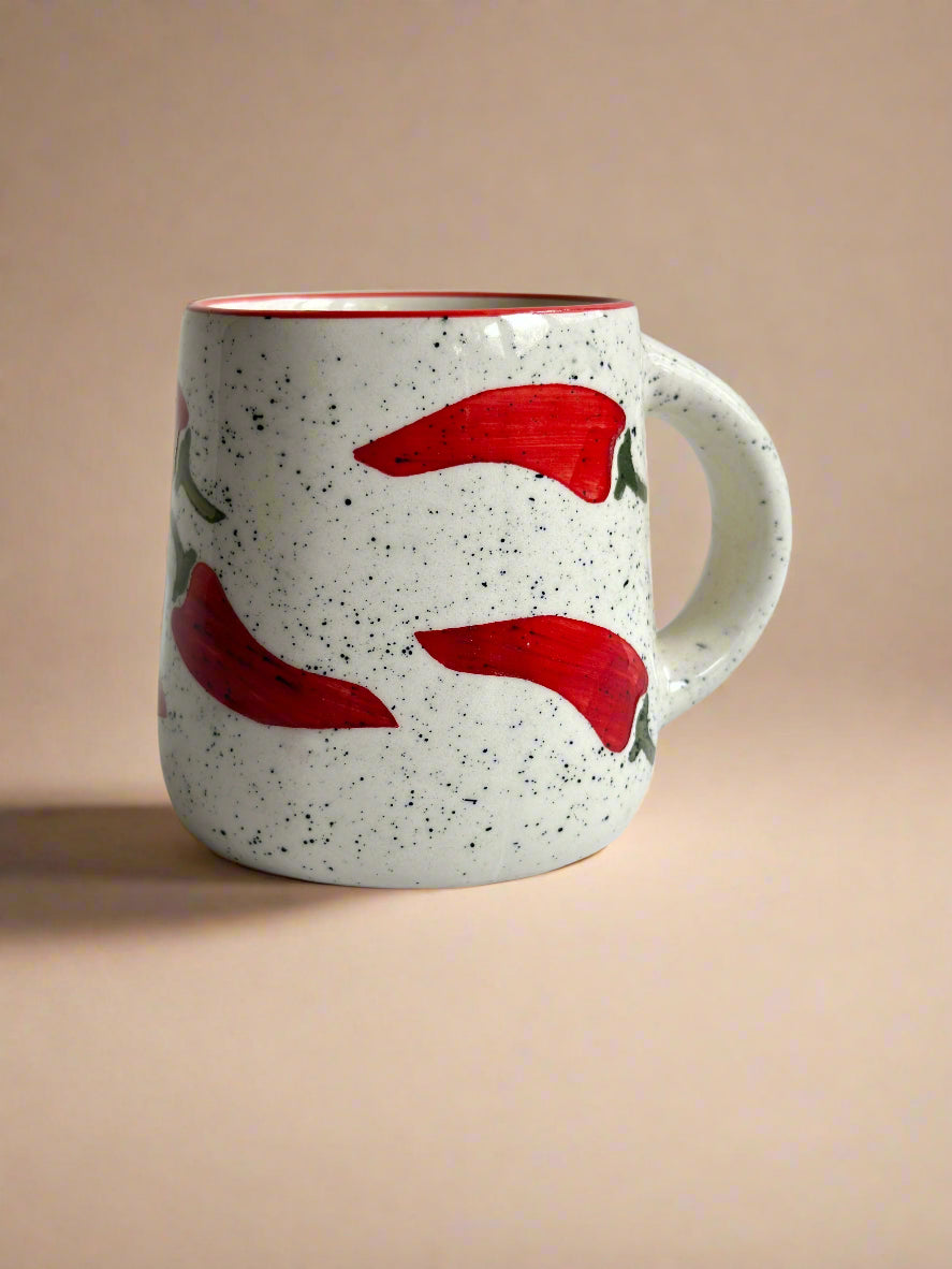 Speckled ceramic mug with red chili pepper design on a beige background