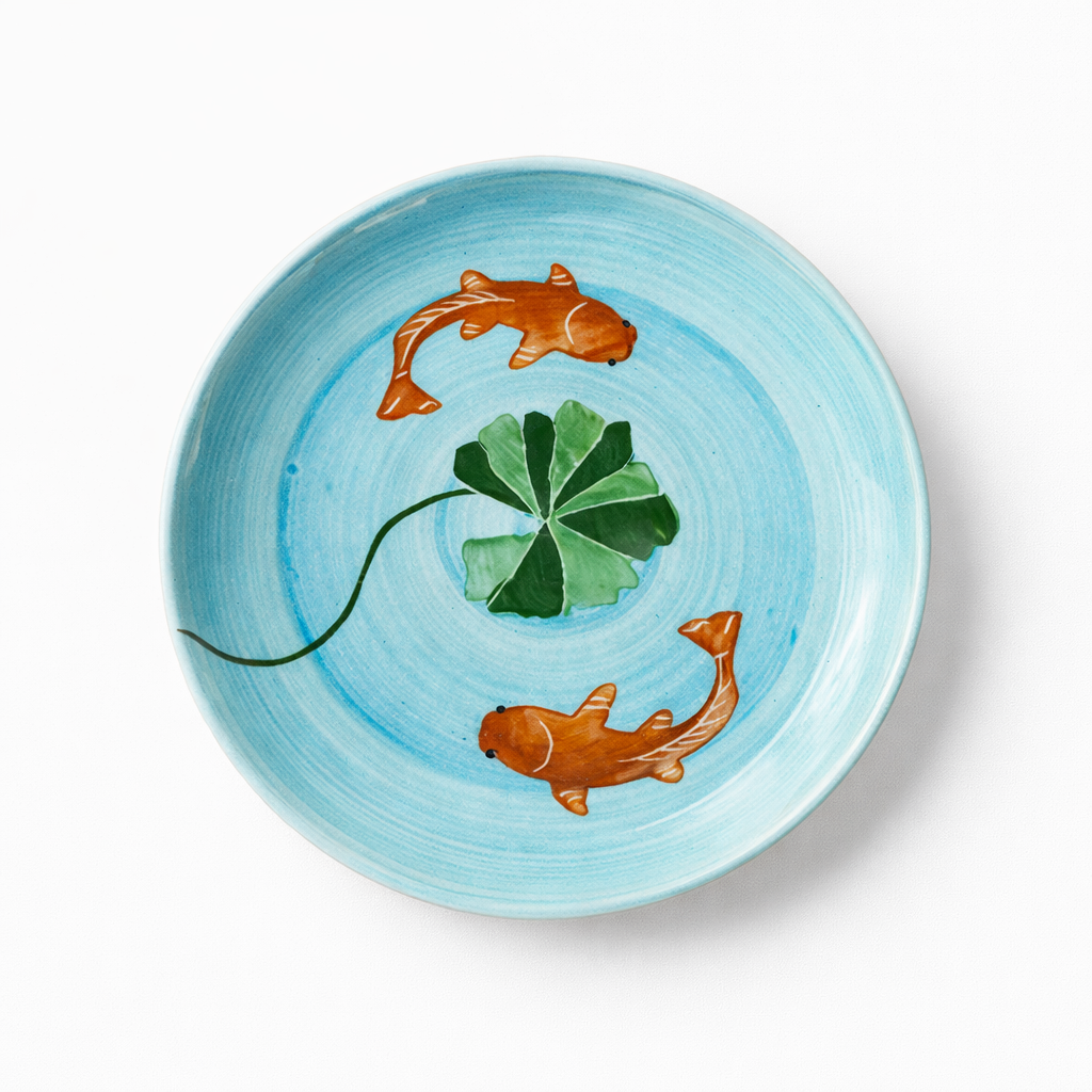 Ceramic plate with hand-painted design of two koi fish and a leaf on a light blue background
