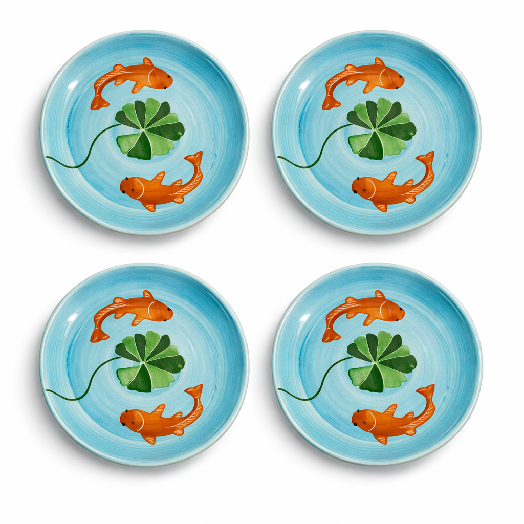 Four ceramic plates with fish and lily pad design on a blue background