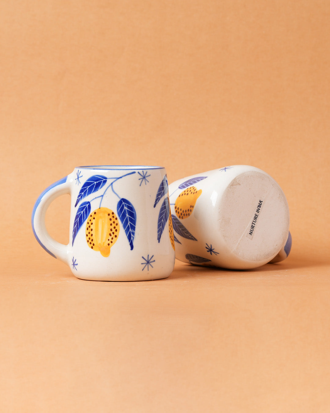 Two ceramic mugs with lemon and leaf designs on a beige background