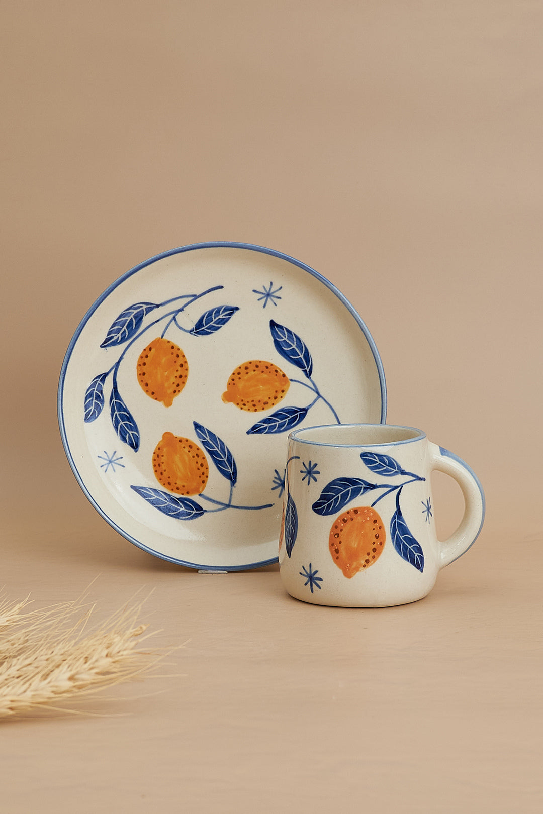 Ceramic mug and plate with orange and leaf design on a beige background