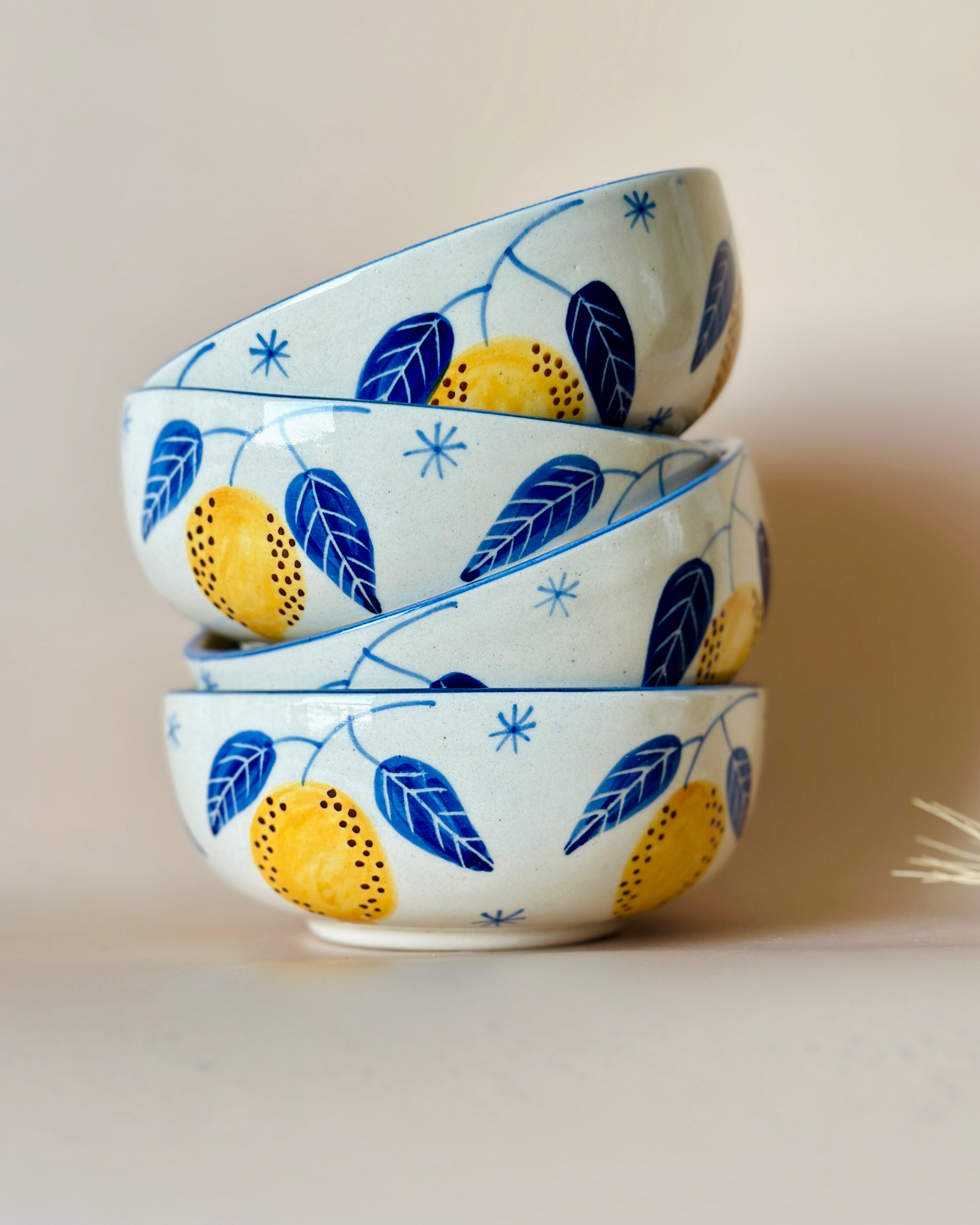 A stack of three ceramic bowls with a handpainted blue and yellow leafy pattern on a sky blue background.