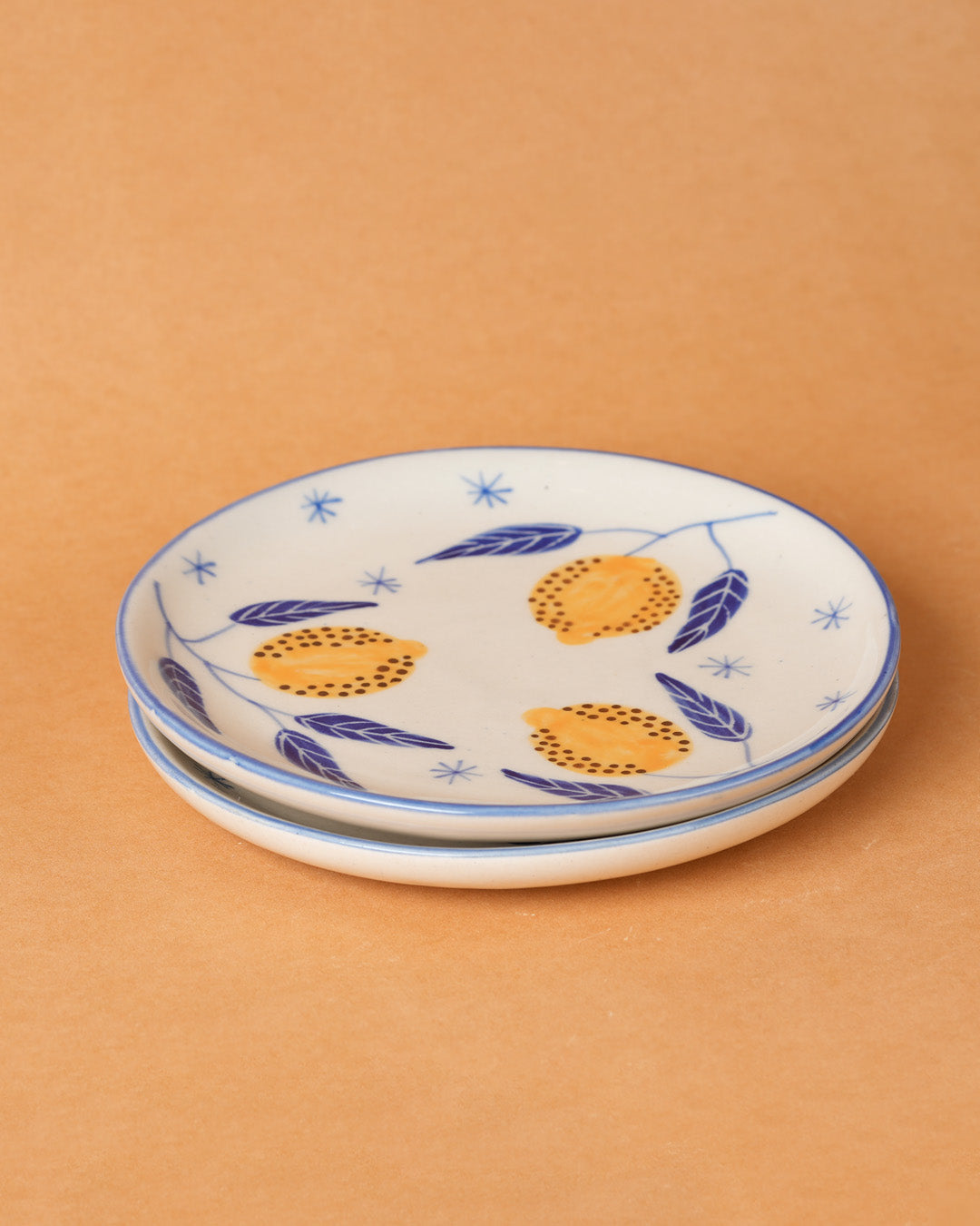 Stack of ceramic plates with orange and blue patterns on a beige background