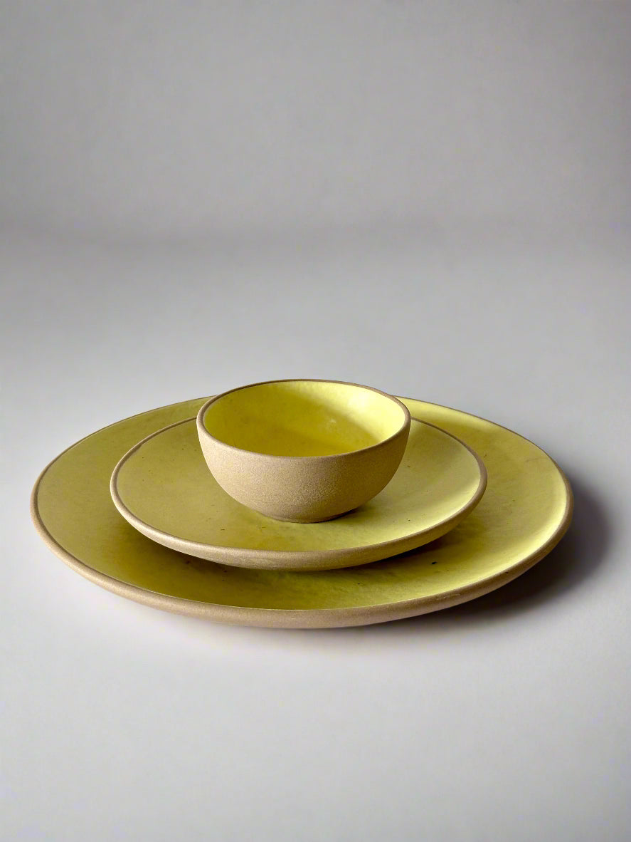 Set of green ceramic plates and bowl on a white surface with a light background