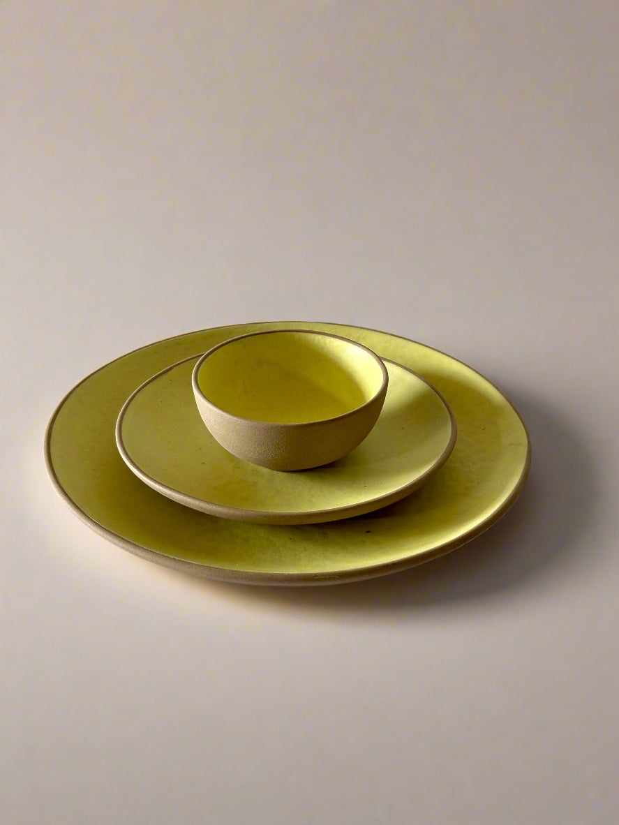 Set of green ceramic plates and bowls on a white surface with a beige wall background