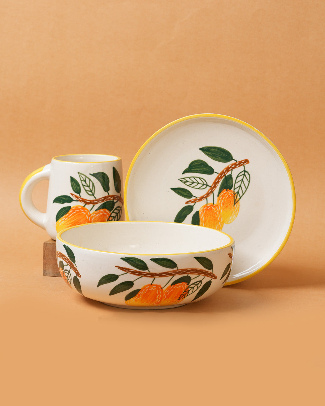 Ceramic set with mug, bowl, and plate featuring orange and leaf design on a beige background