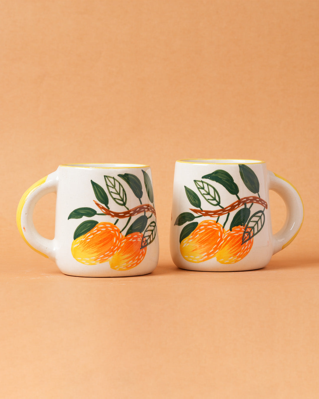 Two ceramic mugs with orange illustrations on a beige background