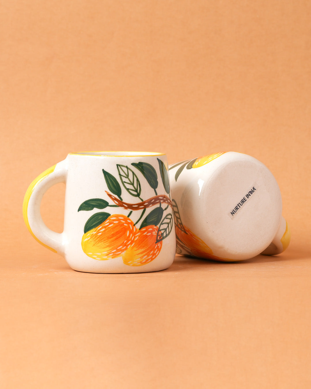 Two mugs on a peach background, one with fruit design and the other plain.