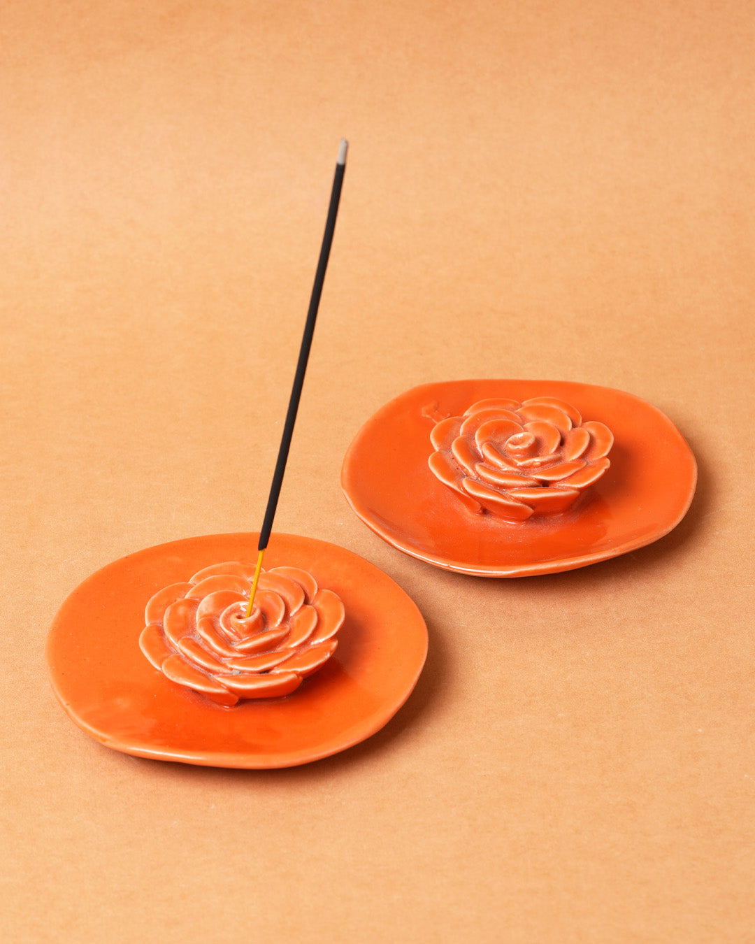 Two orange ceramic incense holders with rose designs on a beige background