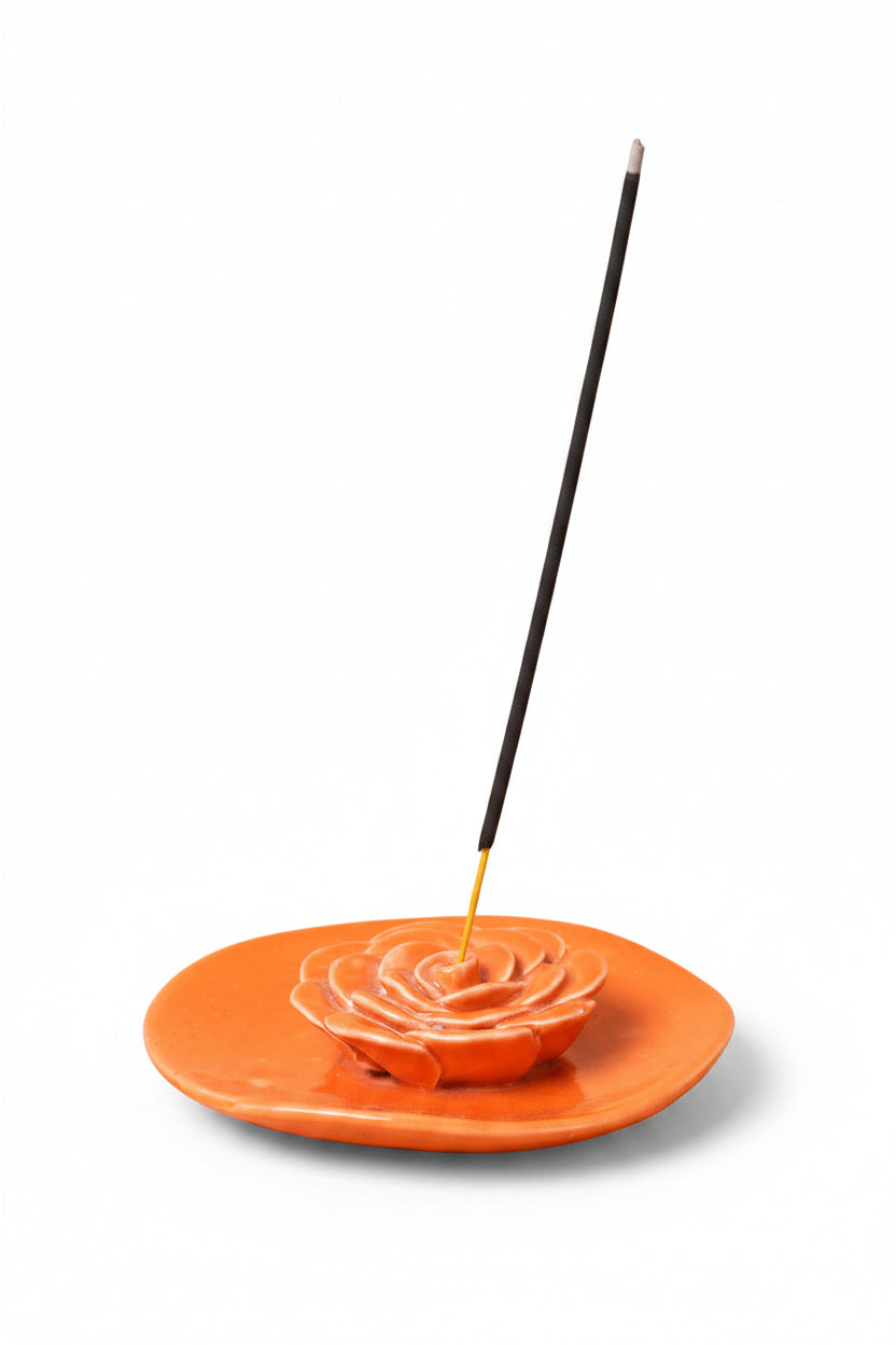 Incense stick on an orange rose-shaped incense holder against a beige background