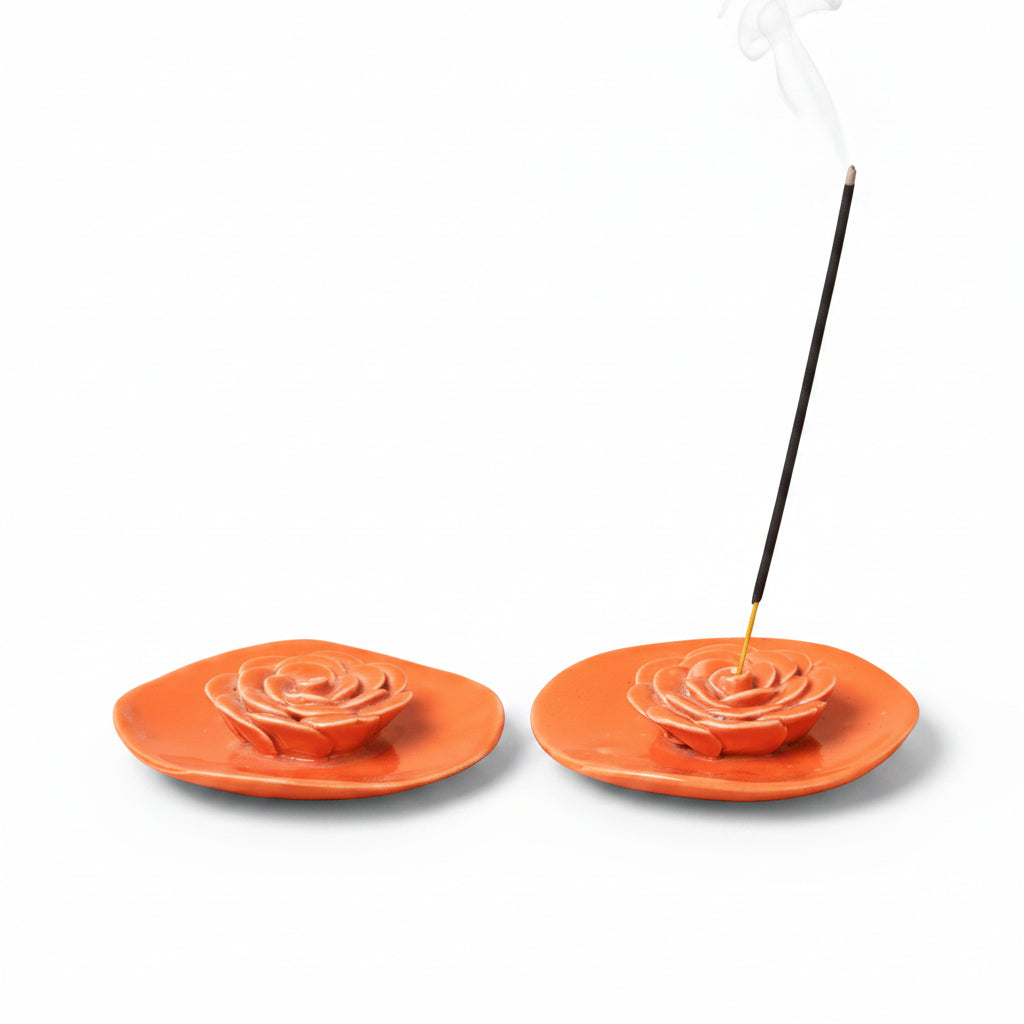 Two orange incense holders with incense sticks on a beige background